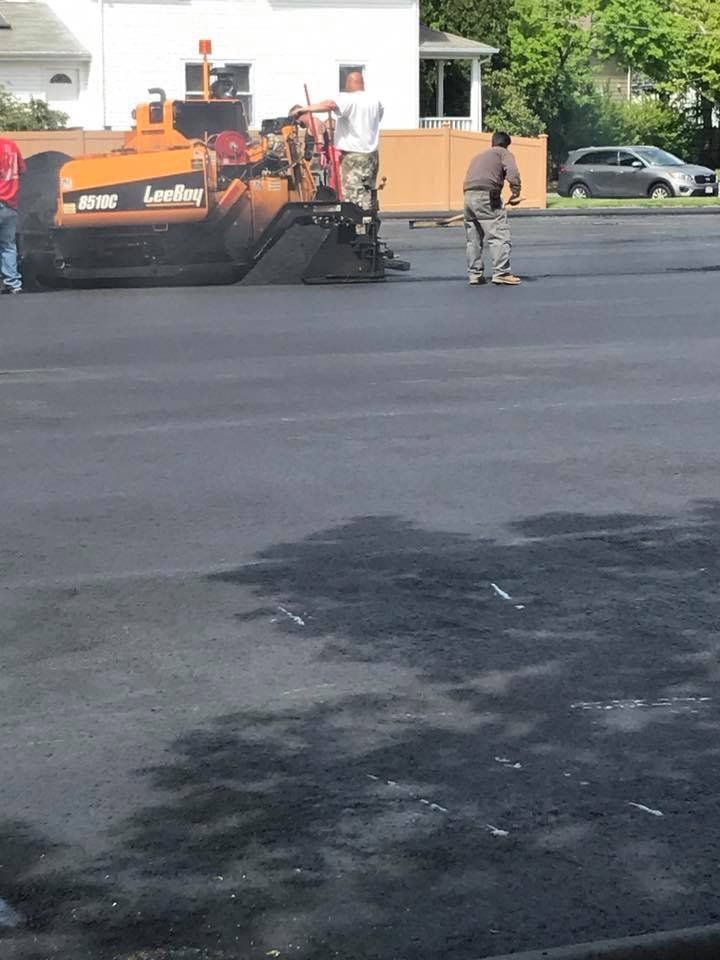 A group of people are standing in a parking lot with a tractor in the background.
