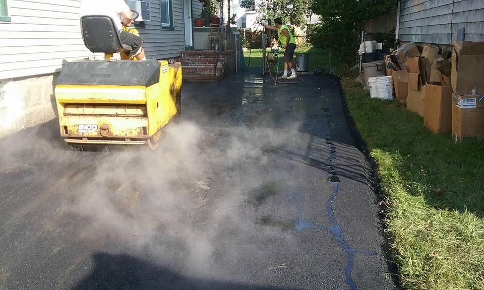 A yellow roller is rolling asphalt in a driveway