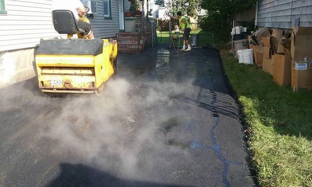 A yellow roller is rolling asphalt in a driveway.