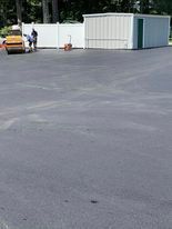 A person is standing in a parking lot with a lawn mower.