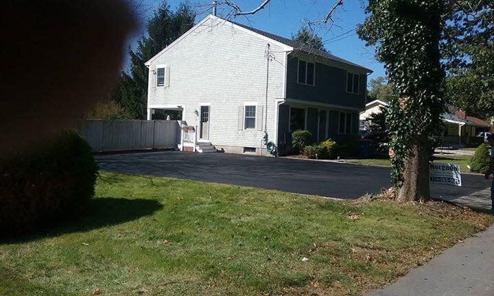 A large white house with a black driveway is sitting on top of a lush green lawn.