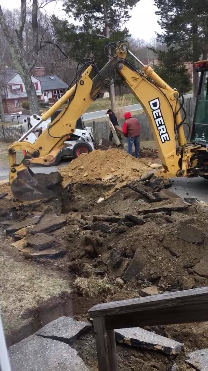 A yellow deere excavator is digging a hole in the ground.