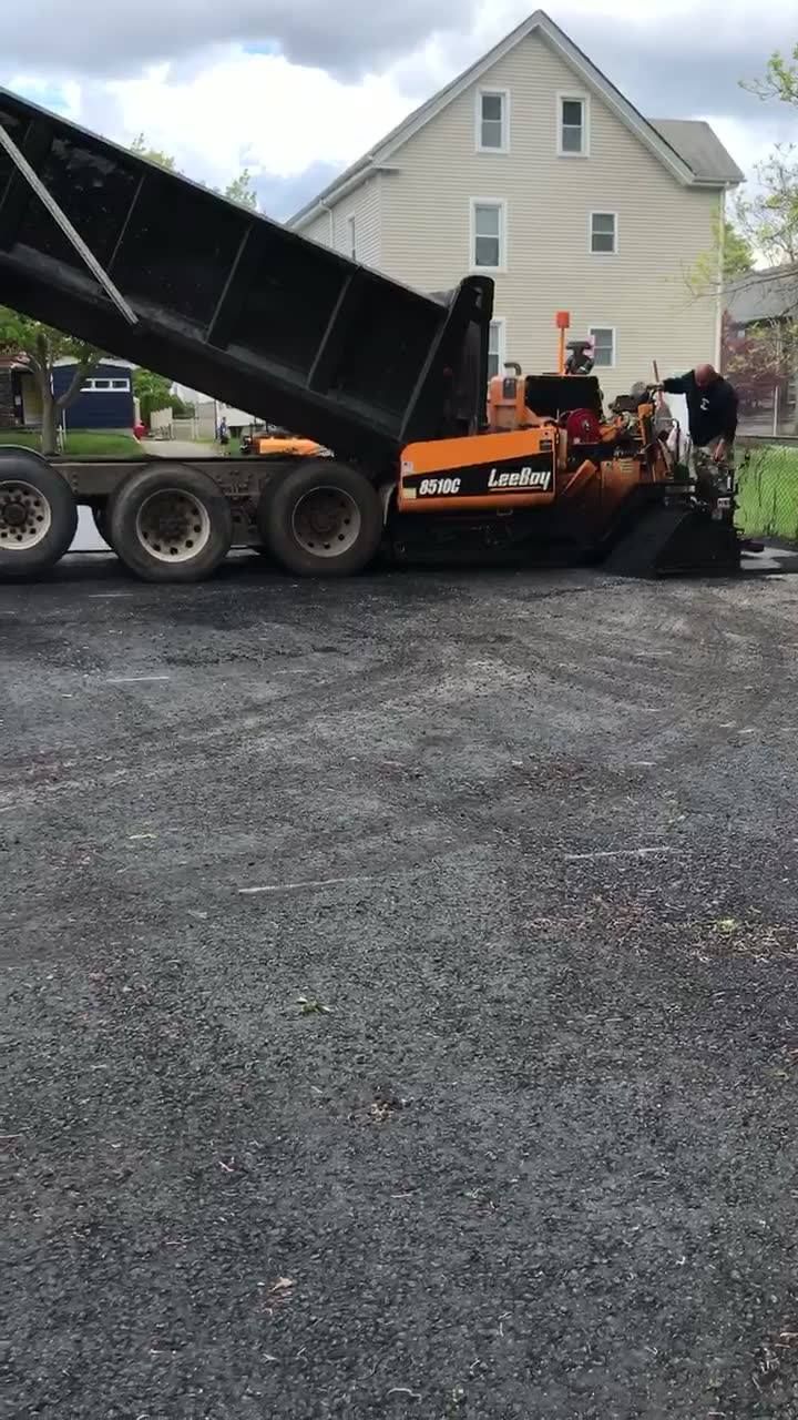 A dump truck is being loaded with gravel in a parking lot.