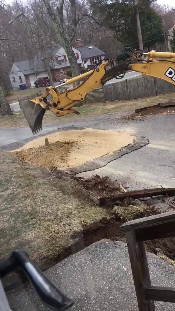 A yellow excavator is digging a hole in the side of a road.