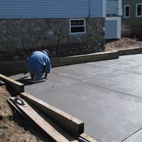 A man is kneeling on a concrete driveway in front of a house.