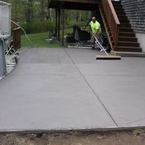 A man is cleaning a concrete driveway with a broom.