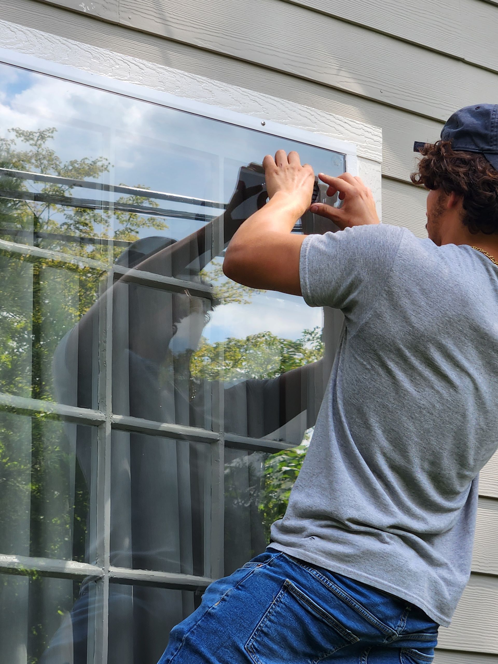 Person hanging a window screen on a white house exterior, seen from behind.