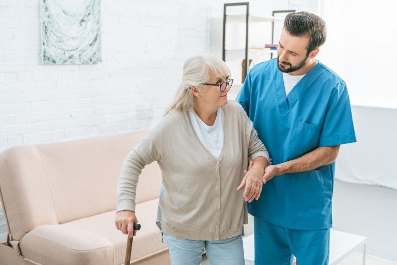 An elderly woman with a cane is being helped by a nurse.