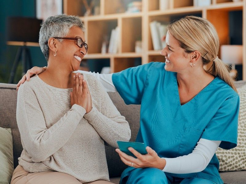 A nurse is sitting on a couch with an elderly woman.