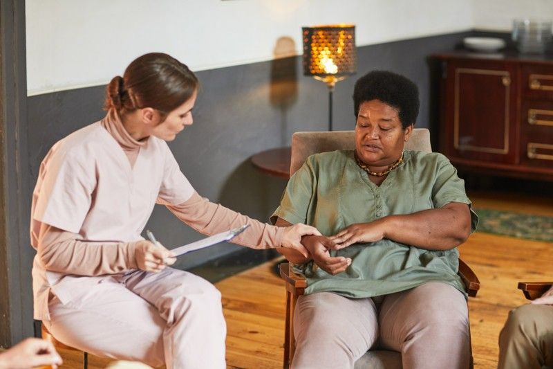 A nurse is talking to an elderly woman sitting in a chair.