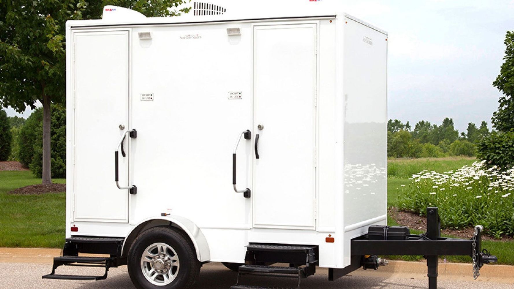 White portable restroom trailer with two separate stalls, parked outdoors.