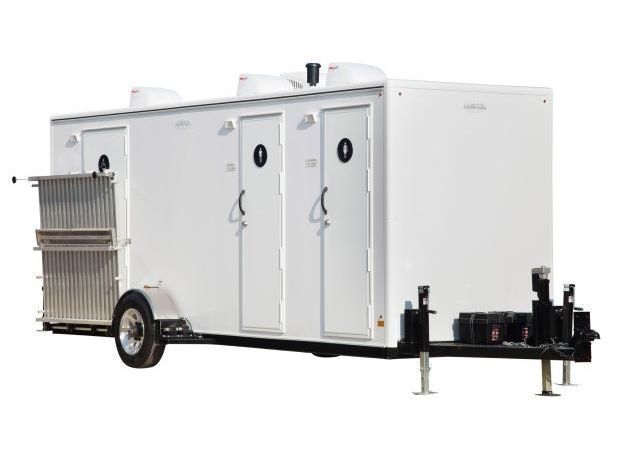 White portable restroom trailer with three stalls and a metal handrail.