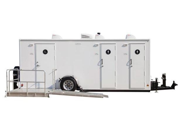 White portable restroom trailer with three stalls, ramp for accessibility, and a black trailer hitch.