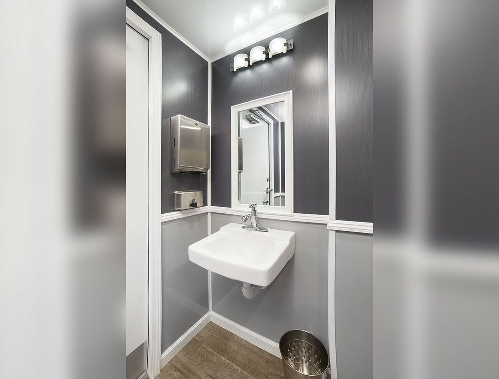 Interior of a small bathroom with a sink, mirror, and paper towel dispenser. Gray walls, white trim.