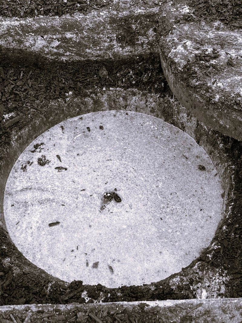 Oval stone set into a dark surface, possibly a well or basin, surrounded by rough stone.