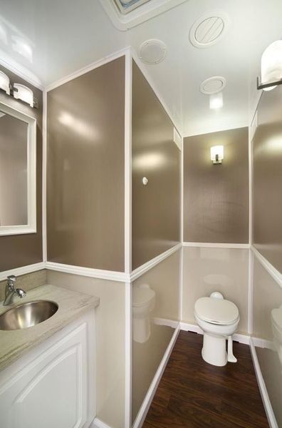 Interior of a luxury portable restroom with a toilet, sink, and decorative lighting.