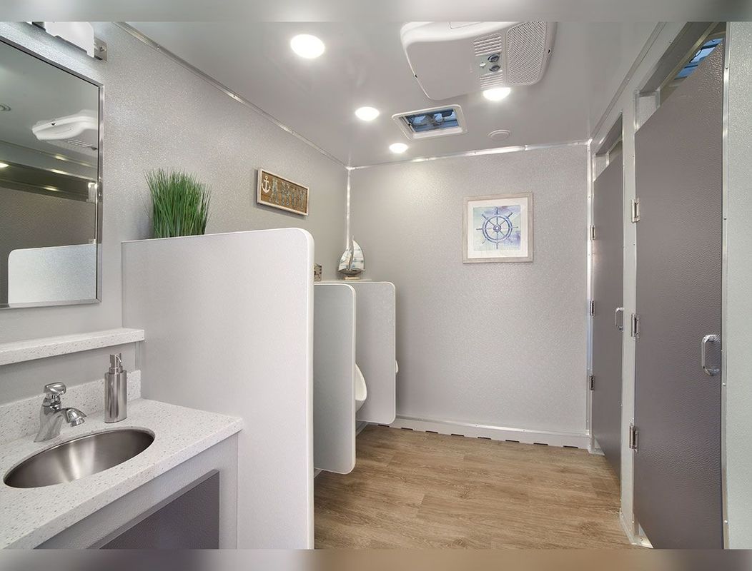 Interior of a modern portable restroom. Features include sink, mirrors, stalls, and potted plant.