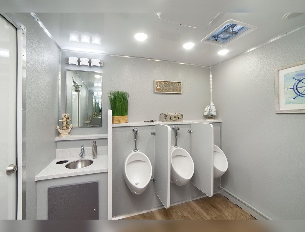 Modern, clean restroom with three urinals, a sink, and a mirror in a well-lit space.
