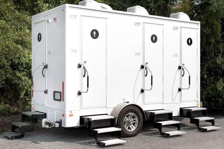 White portable restroom trailer with three stalls, on a trailer with steps.
