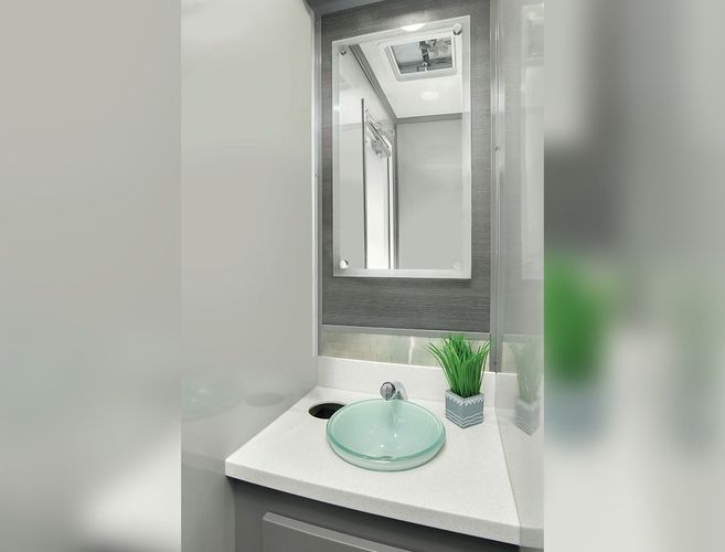 Bathroom with a gray cabinet, white countertop, glass sink, and a framed mirror.