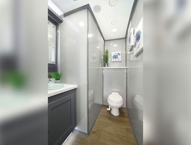 Modern portable restroom interior with toilet, sink, and decorative plants. Gray and white color scheme.