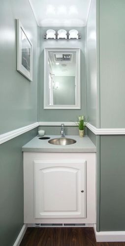 Small bathroom with gray-green walls, white trim and cabinetry, silver sink, mirror, and art.