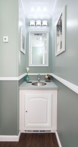 Small, modern bathroom with a white vanity, mirror, and light fixture, in muted green tones.
