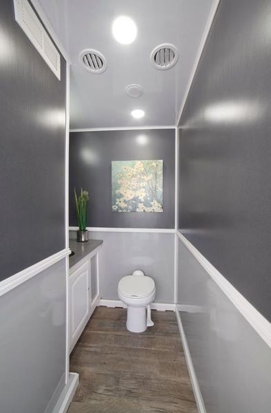 Interior of a portable restroom with gray walls, white trim, a toilet, and a small painting.