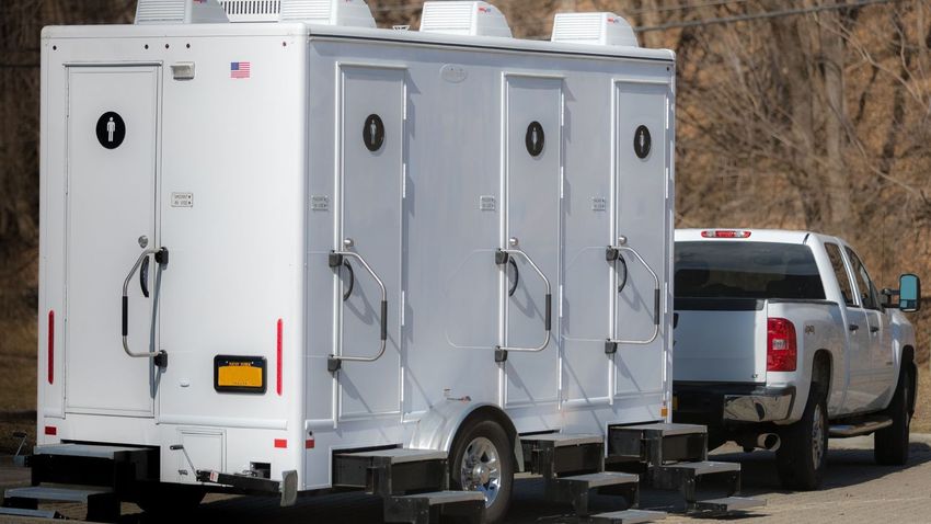 White portable restroom trailer next to a white pickup truck.