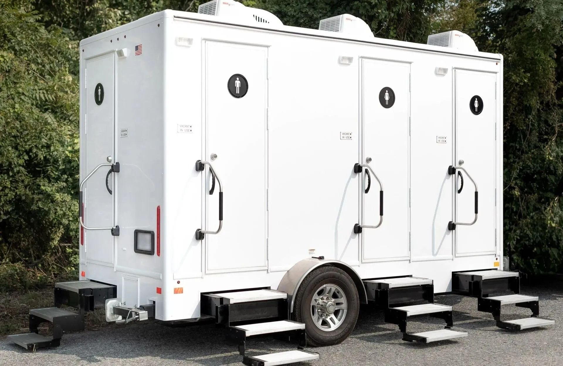 White portable restroom trailer with three individual stalls and steps.