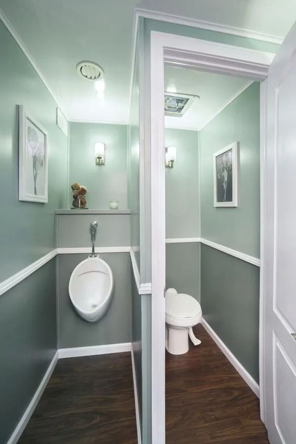 A public restroom with urinal and toilet, divided by a partition, painted in shades of green with white trim.