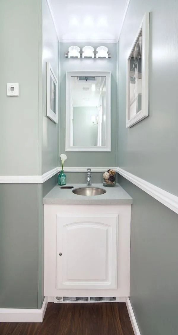 Small, narrow powder room with light blue walls, white trim and cabinetry, and a silver sink.