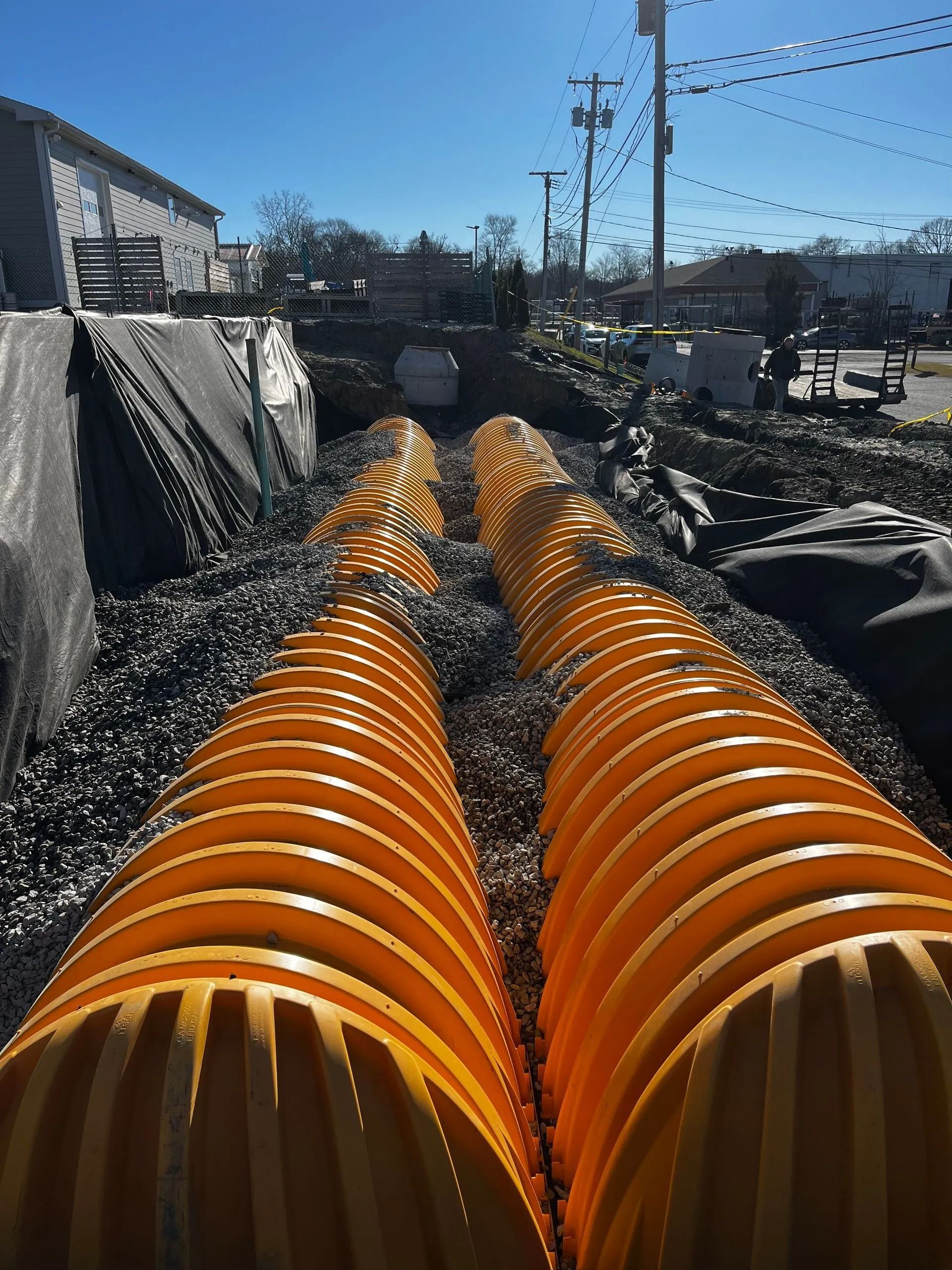 Two parallel rows of large, bright orange plastic corrugated drainage chambers installed in a trench at a construction site.