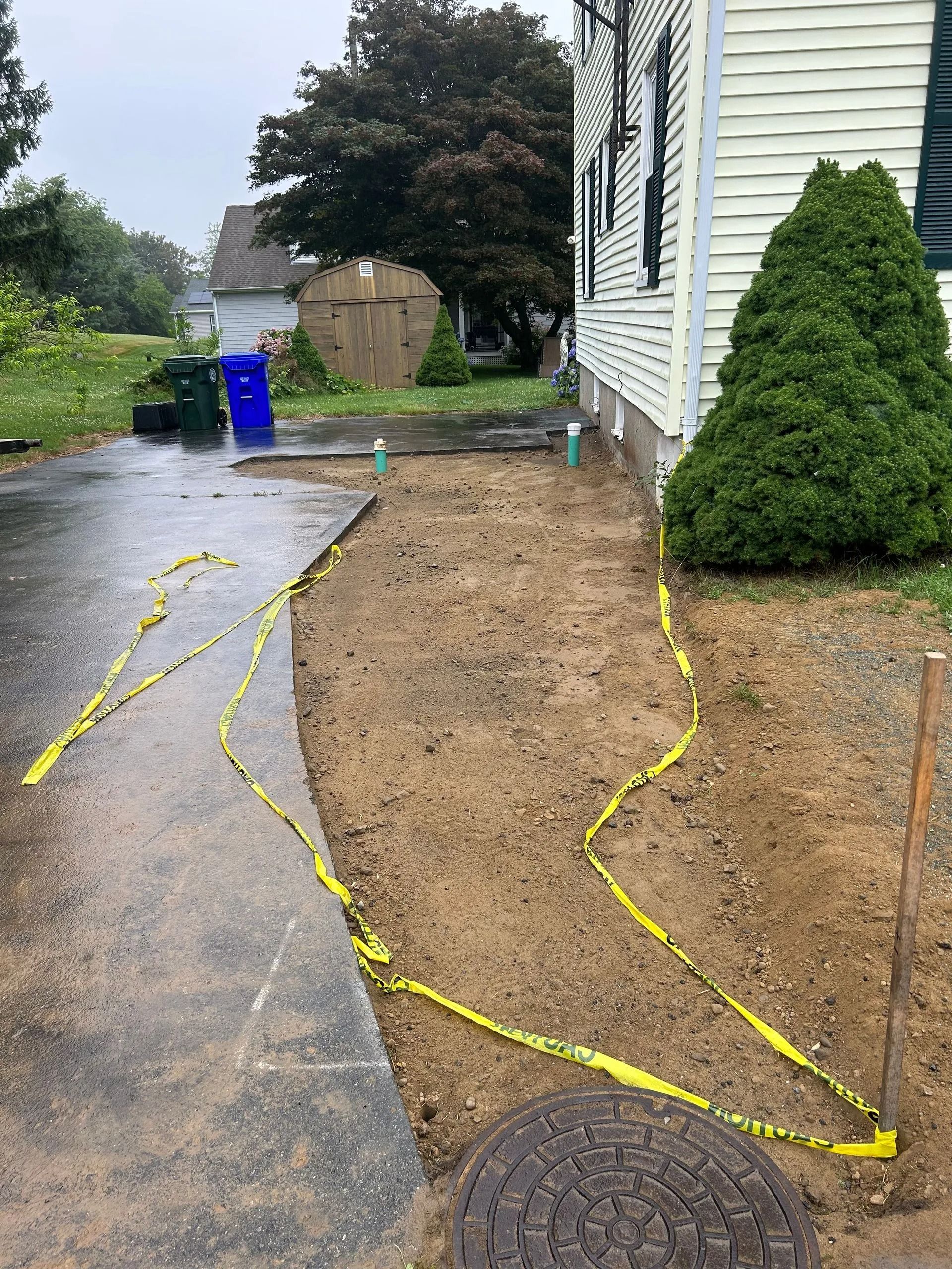 A construction zone featuring a dirt patch beside a house, marked off with yellow caution tape and two green pipes.