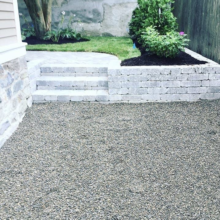 A gravel patio leads to stone steps built into a retaining wall, with a small lawn and garden beds in the background.
