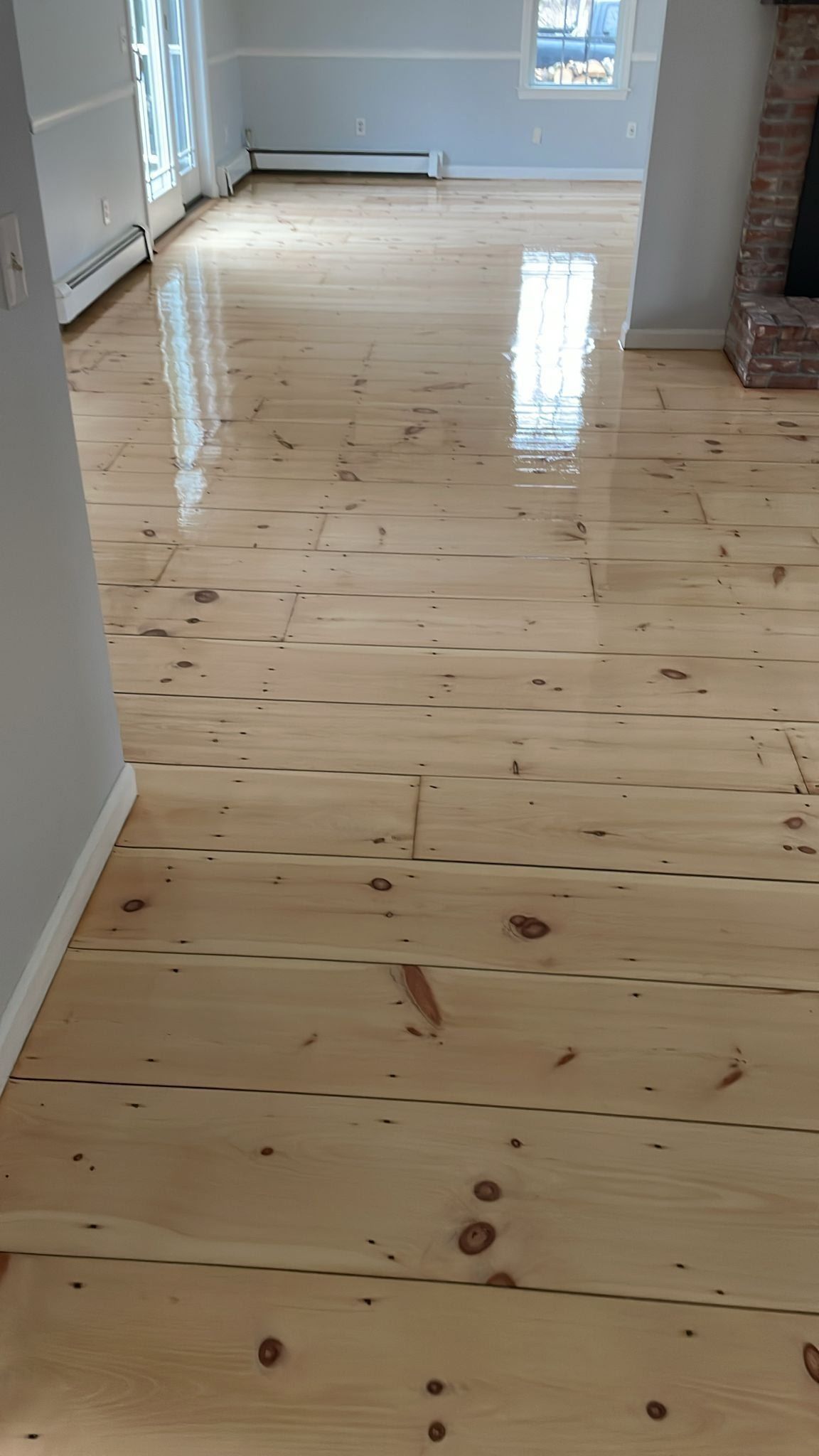 Wood floor in a room, reflecting light. The floorboards are light-colored with dark knots.