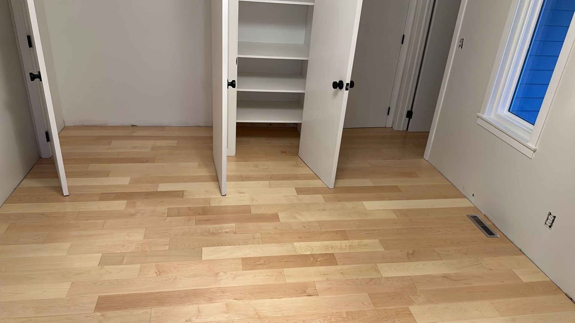 Empty room with light wood flooring, white walls, closet with open doors, and a window.