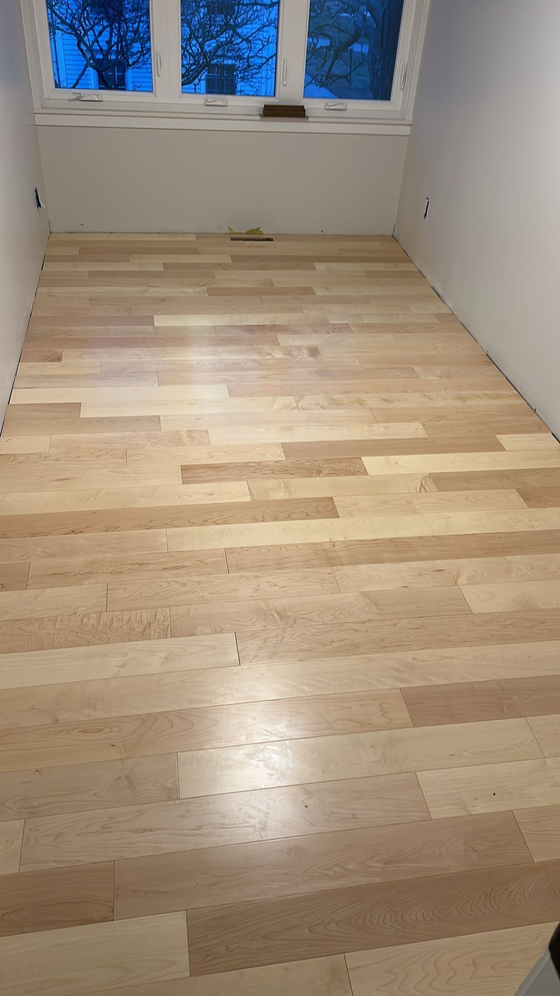 Newly installed light-colored wooden floor in a room with white walls and a window.