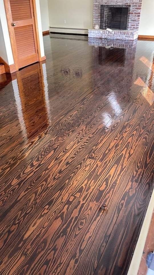 Glossy, dark-stained hardwood floor reflects a fireplace and door; interior setting.