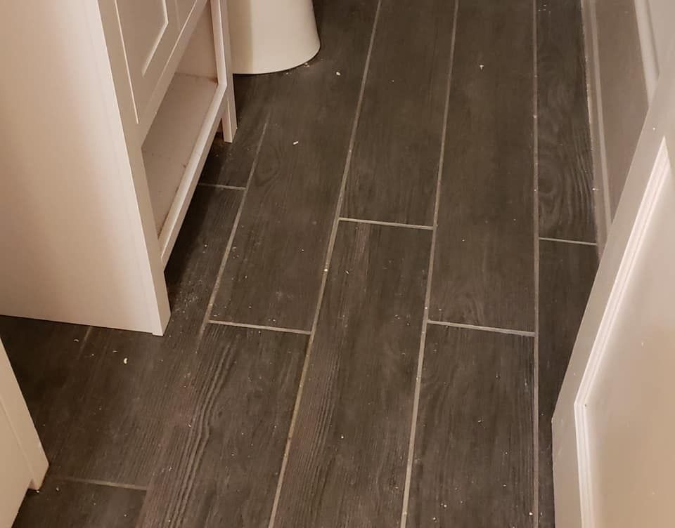 Dark gray rectangular tiles on a bathroom floor, next to white cabinets and a toilet.