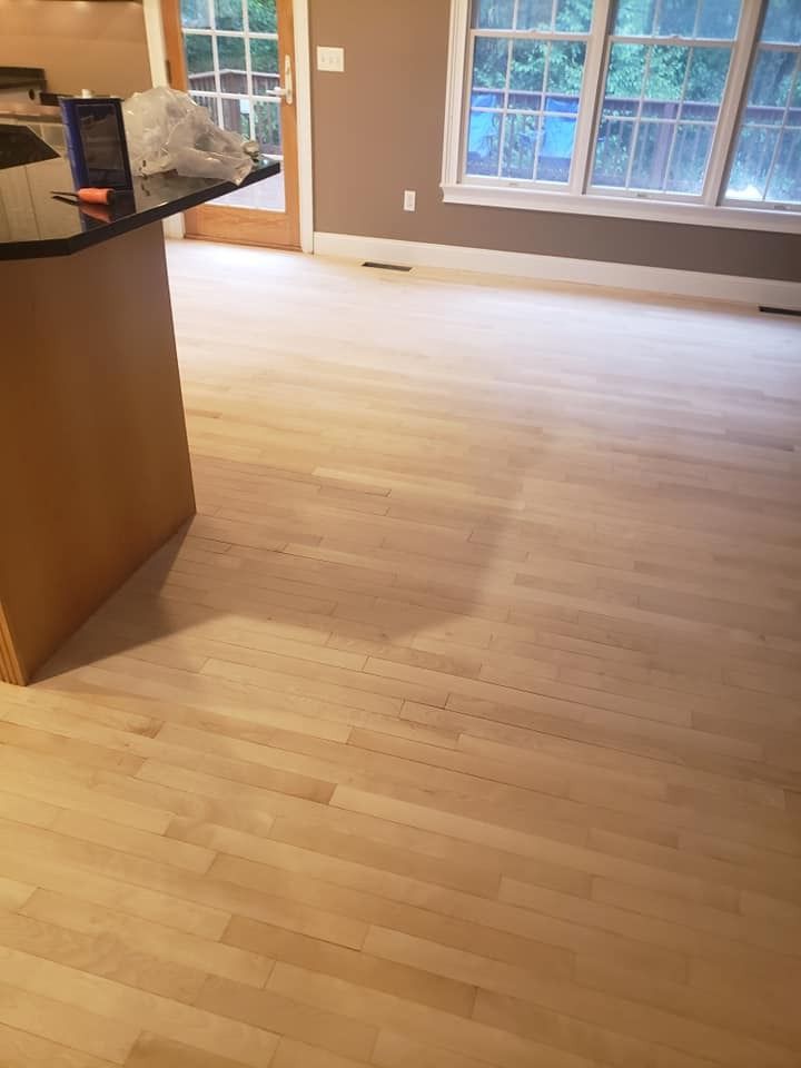 Light-colored hardwood floor in a room with a window, part of a kitchen island on the left.