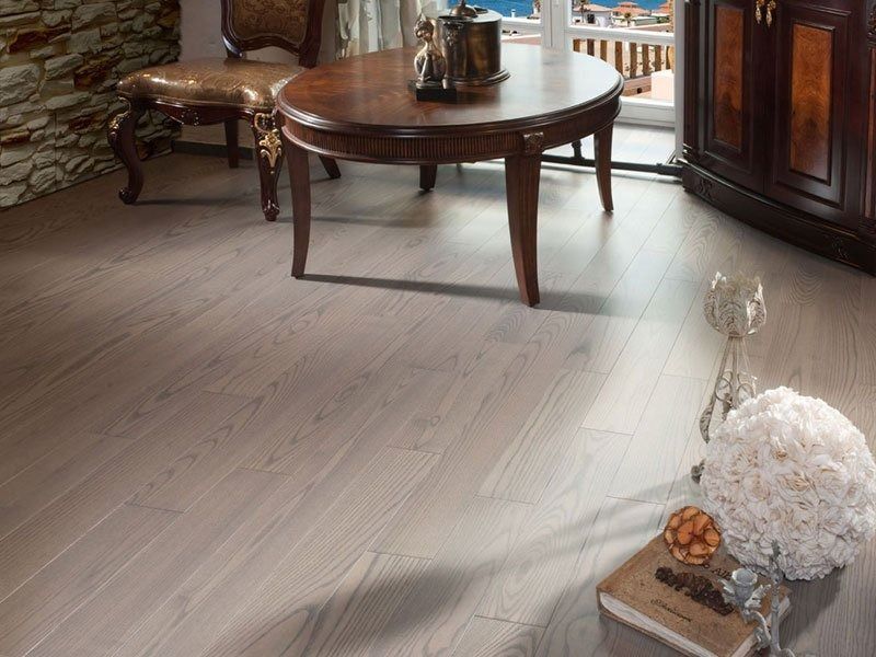 Light wood floor in a room with antique furniture, a round table, and a decorative floral arrangement.