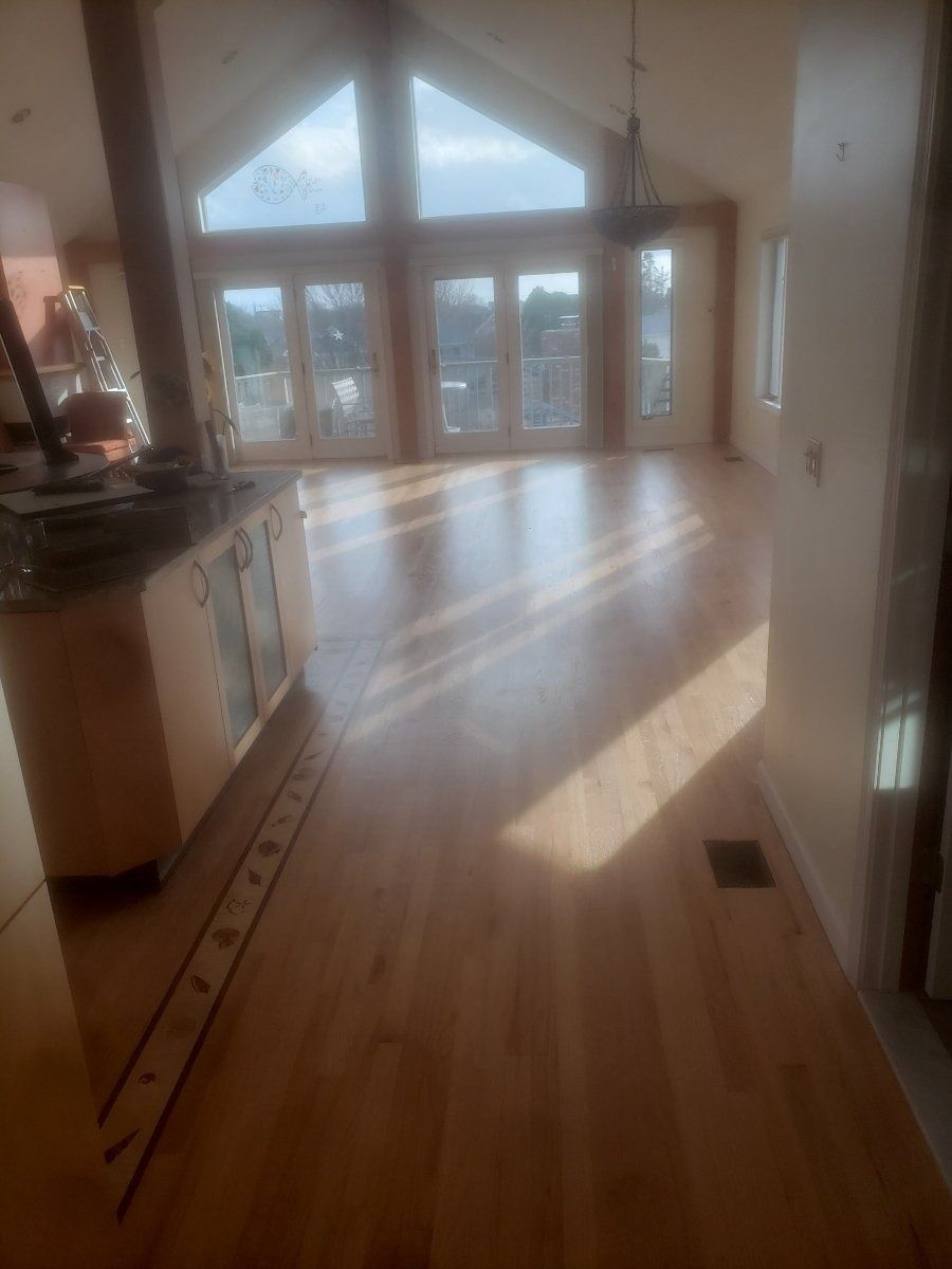 Light-filled interior with newly installed hardwood floors, kitchen counter on the left, and large doors to a balcony in the background.