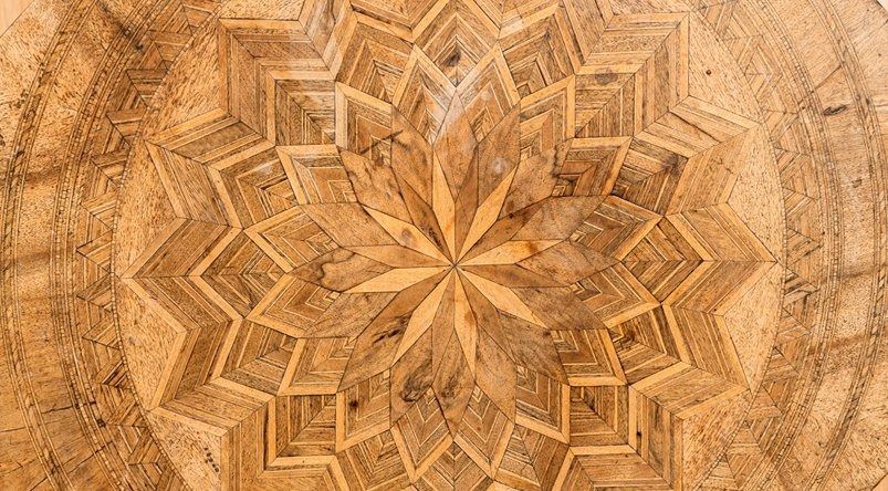 Wooden surface with intricate starburst pattern, light and dark wood in radial design.