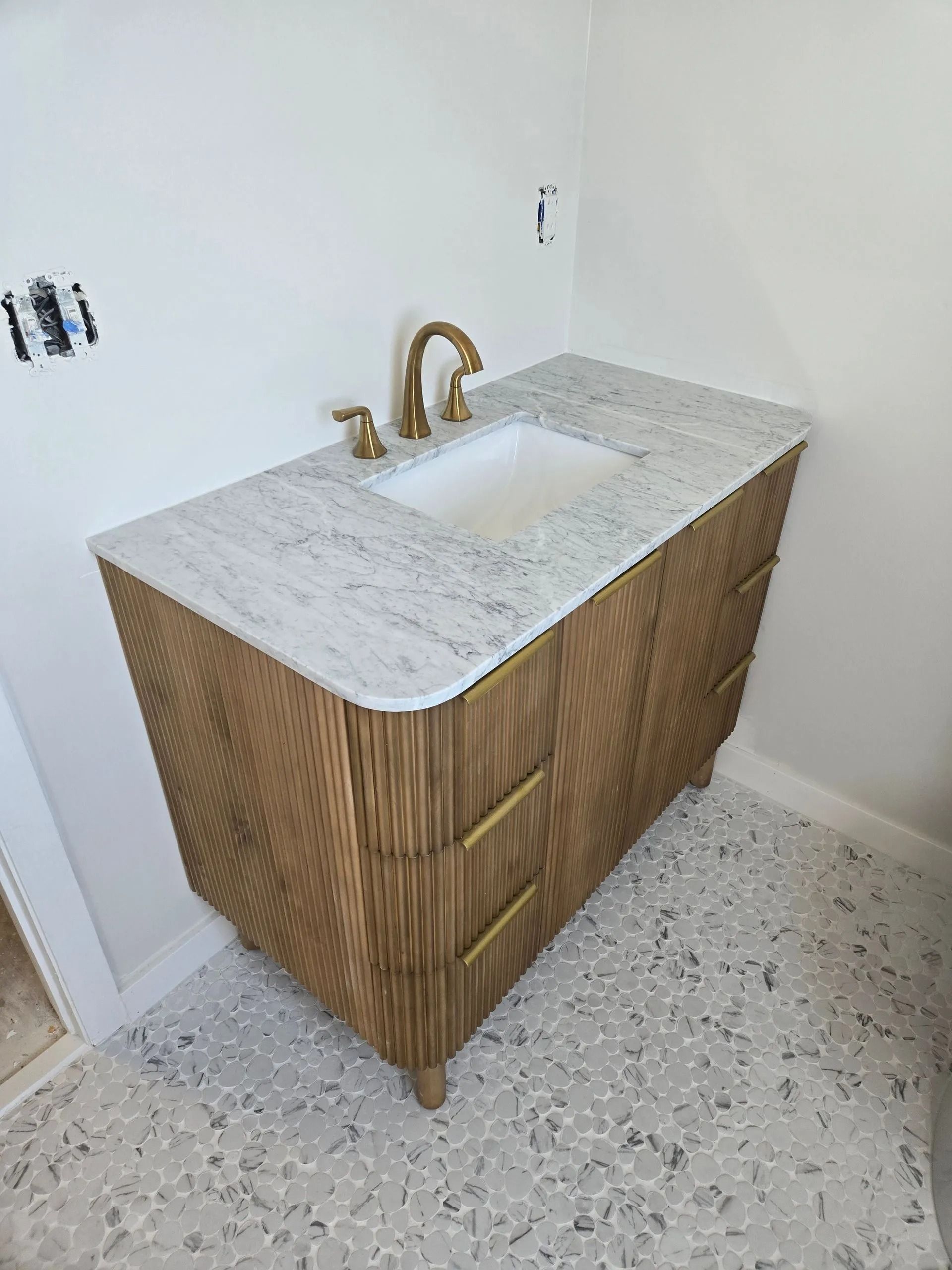 Bathroom vanity with gold hardware, white marble countertop, and textured wood cabinet. Terrazzo flooring.