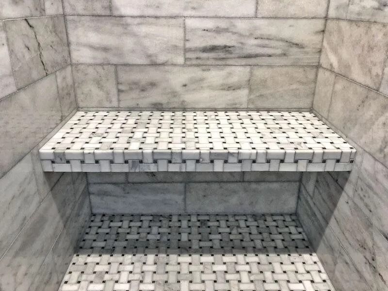 Shower interior with marble tile walls and a built-in bench covered in small, woven-pattern tiles.