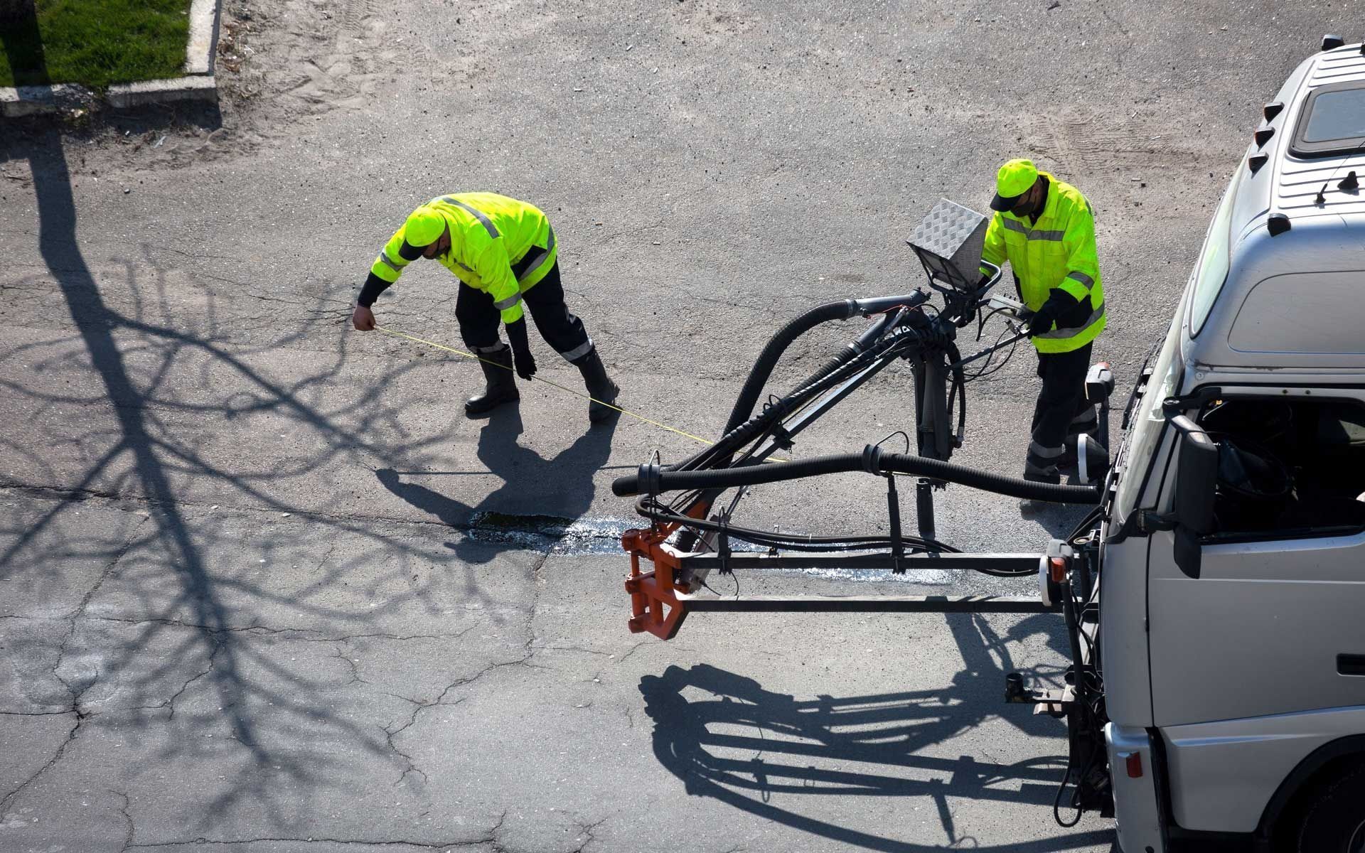Two workers in neon vests loading a bicycle onto a truck in an outdoor setting.
