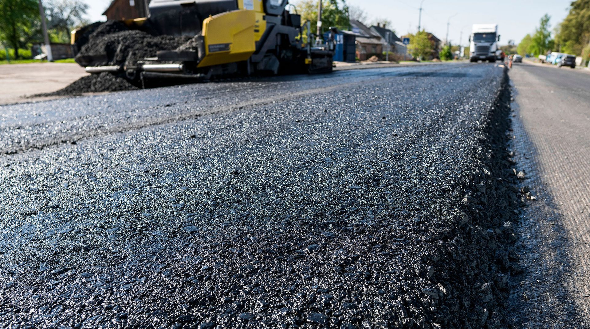Asphalt road resurfacing in progress; a yellow paver lays fresh black asphalt.