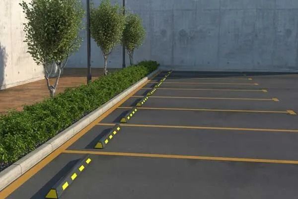 Parking lot with yellow painted lines and parking stops, lined with shrubs and trees.