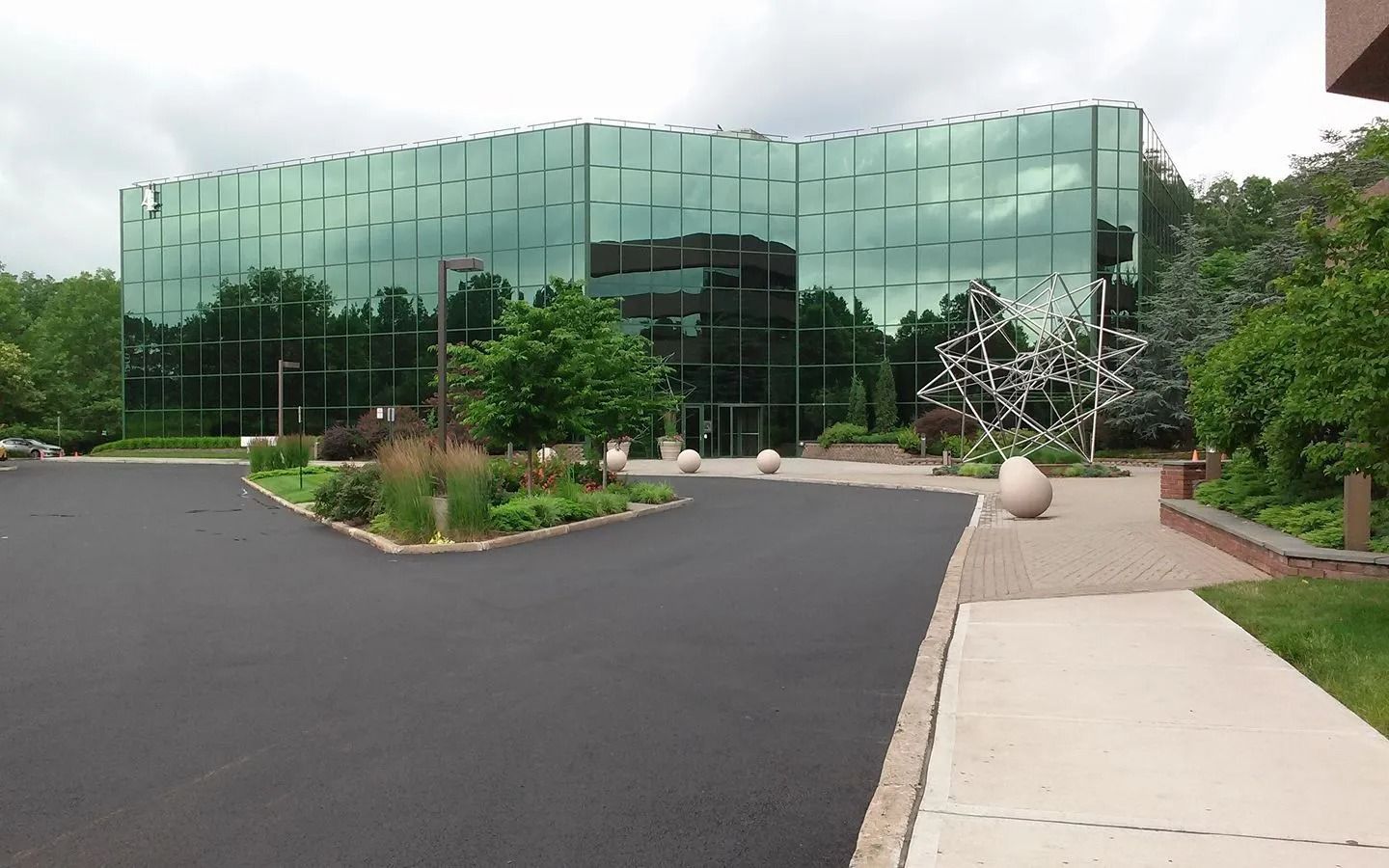 Glass-walled modern office building with landscaping, a sculpture, and a paved entrance.